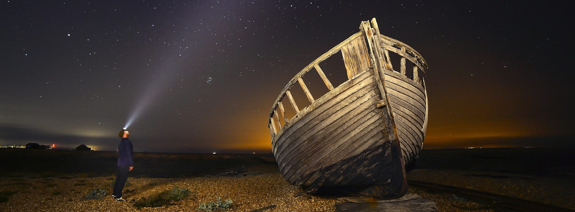 man standing beside brown wooden boat under starry night